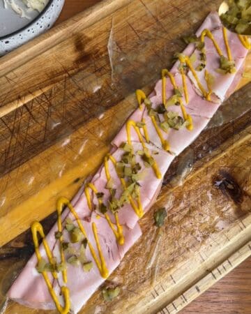 the making of a crispy cuban rice paper sandwich, with ham, mustard, and roasted pork on rice paper on a cutting board