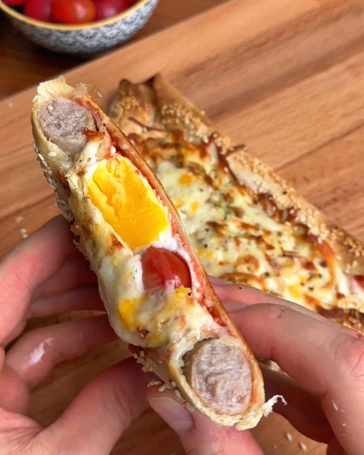 a sliced piece of a tortilla breakfast pizza with sausage stuffed crust, with soft egg yolk, marinara and melty cheese