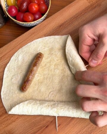 breakfast sausages being rolled into the edges of a tortilla, in prep for a breakfast pizza with sausage stuffed tortilla crust