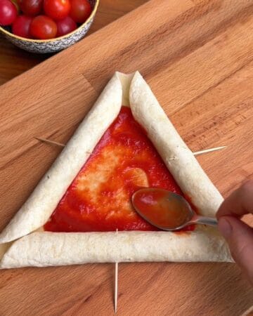 marinara being spread in the center of a tortilla, with sausages rolled into the tortilla around it, in prep for a breakfast pizza with sausage stuffed tortilla crust