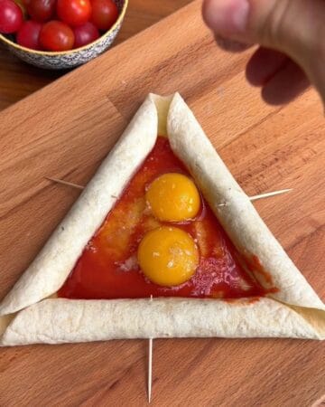 two egg yolks in the center of a tortilla, with sausage rolled into the crust, in prep for the making of a tortilla breakfast pizza with sausage crust