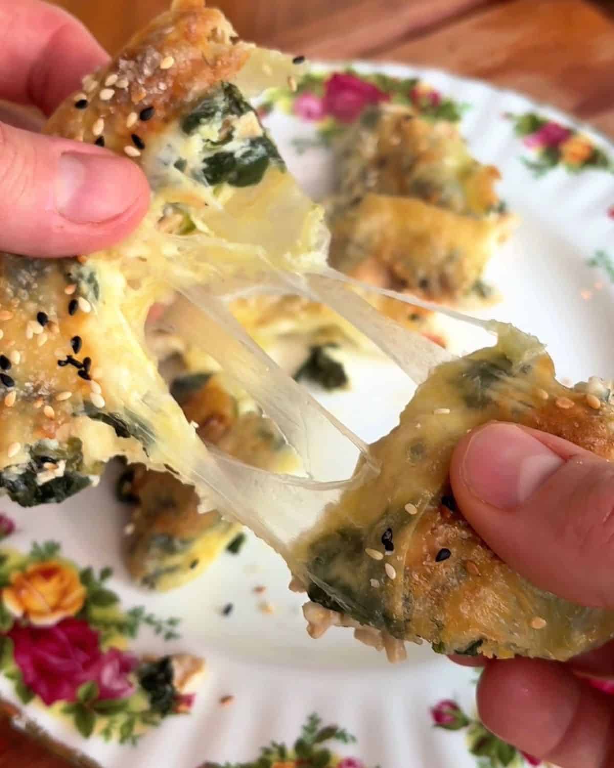 the insides of a rice paper spanakopita being pulled apart to reveal melty cheese, spinach and chicken inside