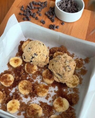 sliced bananas on a cookie sheet, sprinkled with brown sugar, and batter, for the making of caramelized banana chocolate chunk blondies