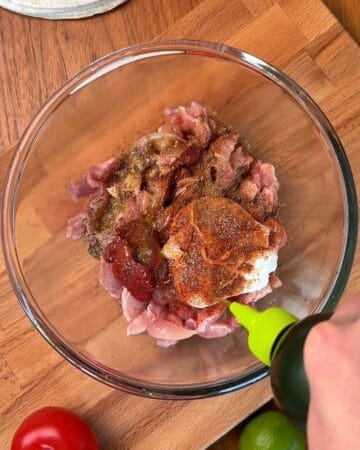 chicken in a bowl, being marinated with oil, spices, and herbs, for the making of a chicken shawarma wrap