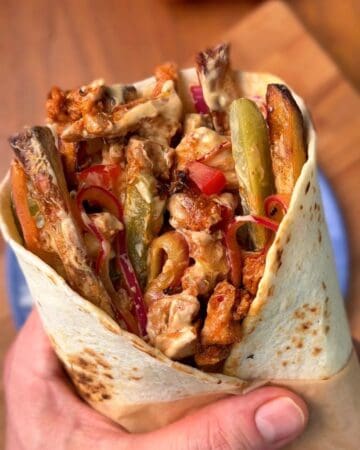 a juicy chicken shawarma wrap featuring a garlic yogurt sauce, pickled red onions and french fries wrapped inside