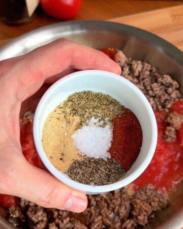 seasonings in a dish being added to a pan of beef and fresh tomatoes for the making of creamy ground beef pasta made with fresh tomatoes