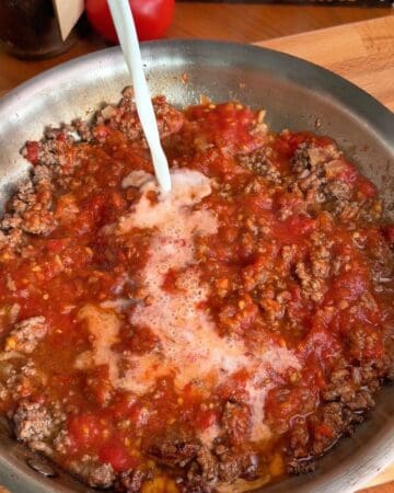 skim milk being added to a pan of tomato beef sauce