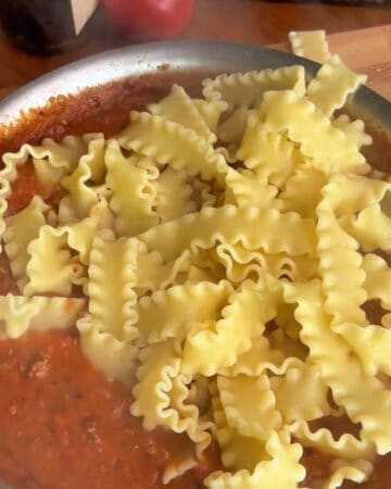 fresh pasta being added to a a pan of beef sauce for creamy ground beef pasta made with fresh tomatoes