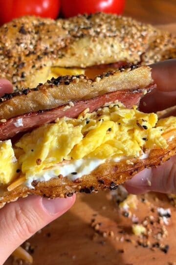 crispy rice paper bacon egg and cheese sandwich sliced in half, so the layers of bacon, egg, cream cheese and cheddar are visible