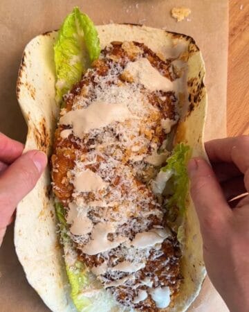 hot honey cornflake chicken Caesar wrap begin assembled with lettuce, parmesan, crispy cornflake chicken, Caesar dressing, and hot honey