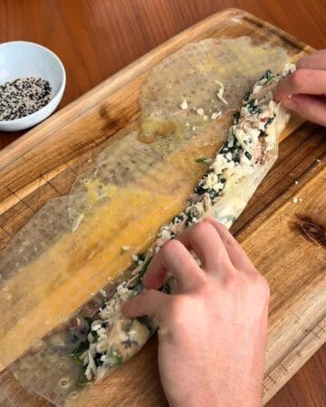 spanakopita filling, with feta cheese, spinach, and chicken, being rolled into rice paper for a rice paper spanakopita spiral
