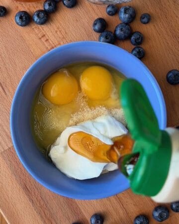 Eggs and milk in a blue bowl with blueberries on a wooden surface.