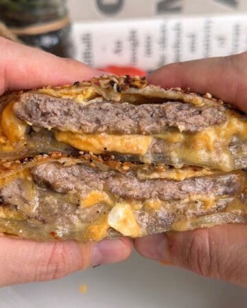 a breakfast sandwich wellington, sliced in half so the inside layers are visible, with melty cheese and sausage juices dribbling out