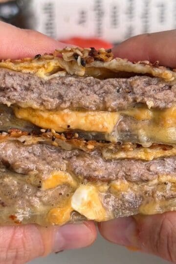 breakfast sandwich wellington sliced in half so layers are visible, with melty cheese, juicy sausage patty, and runny egg