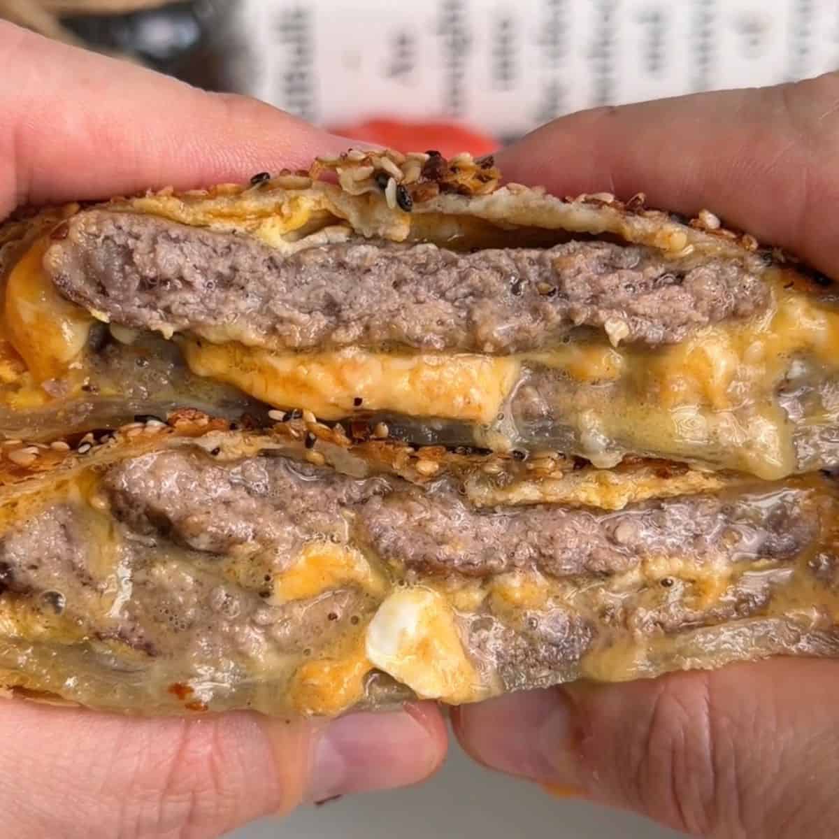 breakfast sandwich wellington sliced in half so layers are visible, with melty cheese, juicy sausage patty, and runny egg