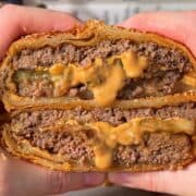 crispy cheeseburger wellington sliced in half so the melty cheese, pickle and juicy beef is visible