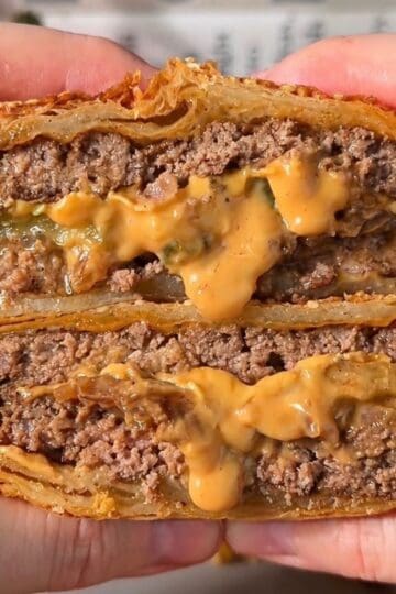 crispy cheeseburger wellington sliced in half so the melty cheese, pickle and juicy beef is visible