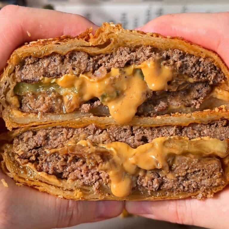 crispy cheeseburger wellington sliced in half so the melty cheese, pickle and juicy beef is visible