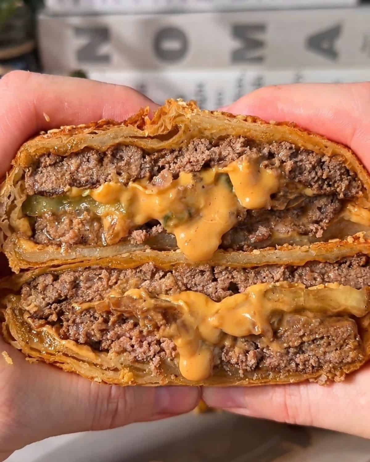 cheeseburger wellington sliced in half, with melted cheese, pickle juice, and juicy beef dripping out