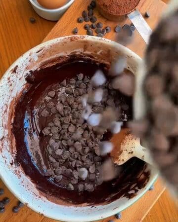 chocolate chips folded into fudgy brownie cookie batter in a white bowl