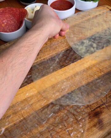 rice paper sheets being laid out on a cutting board in prep for the making of a pepperoni pizza rice paper spiral