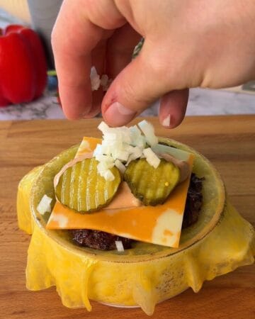 Rice Paper Cheeseburger Wellington being built in a bowl with burger patties, cheese, pickles and onions