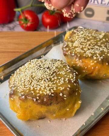 Delicious Rice Paper Cheeseburger Wellingtons topped with sesame seeds, melted cheese, and savory beef patties on a baking tray.