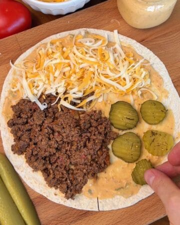 burger sauce, ground beef, shredded cheese, and pickles, laid out on a flour tortilla ready to be folded and cooked for a crispy smashburger quesadilla