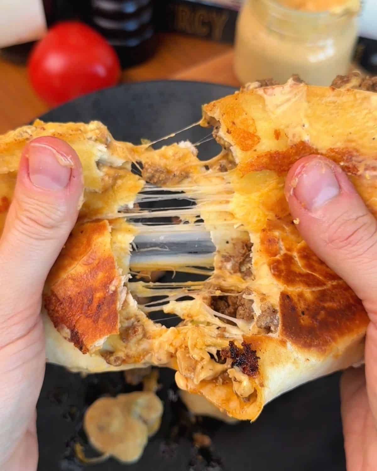 a crispy smashburger quesadilla being pulled apart so the inside is visible, with melty cheese strings and juicy ground beef