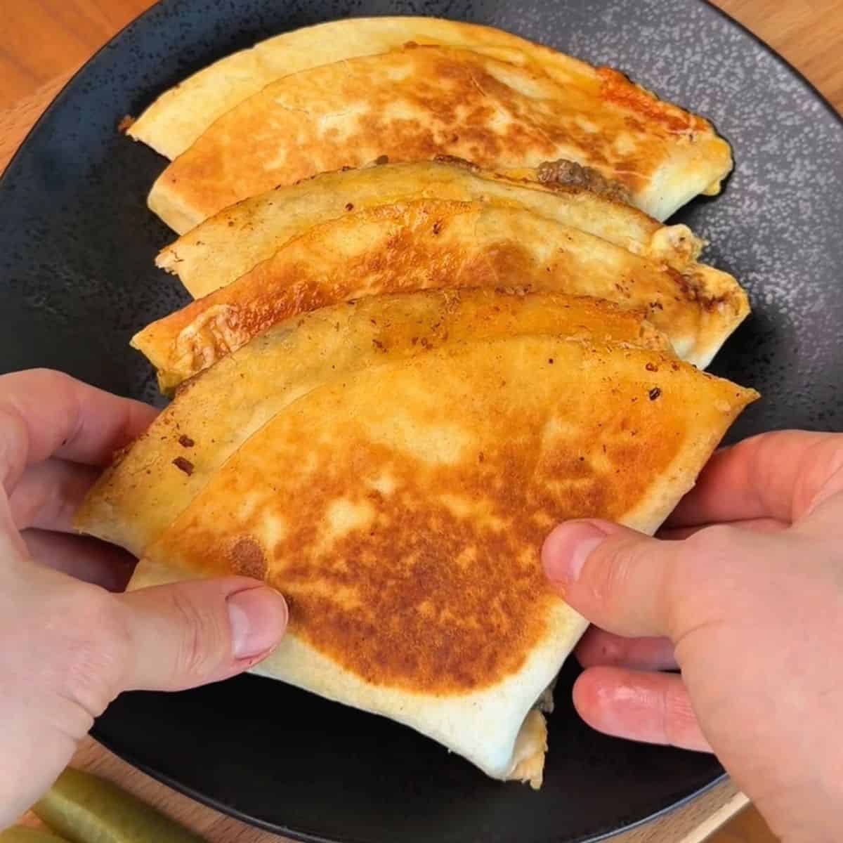 a plate of golden brown, folded crispy smashburger tortillas stuffed with beef and cheese ready to be eaten