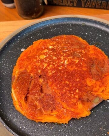 a crispy, cheesy, sweet potato pancake being fried in a frying pan