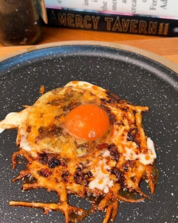 an egg frying on top of a pile of cheese, crisping up to be added to the top of a crispy smashed sweet potato pancake