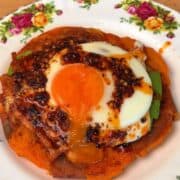 a crispy smashed sweet potato on a plate, layered with avocado, a funny egg, and topped with chili crisp