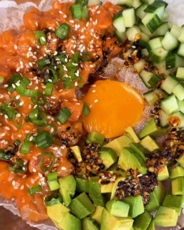 a spicy salmon tostada with avocado, green onion, sesame seeds, and egg yolk