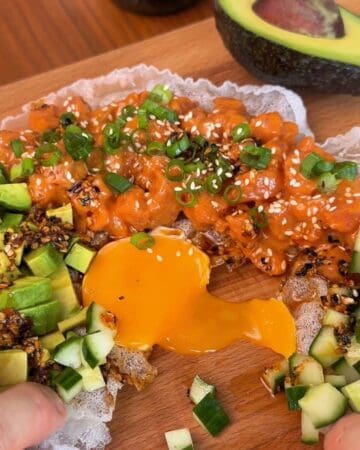 dripping egg yolk on a rice paper tostada, topped with cucumber, avocado, spicy salmon, green onion and sesame seeds