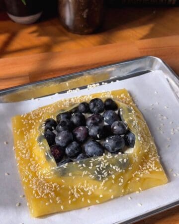Blueberry danish made in rice paper and topped with sesame seeds on a metal tray.