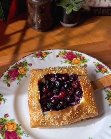 Blueberry rice paper danish with sesame seed crust on floral plate, close-up.