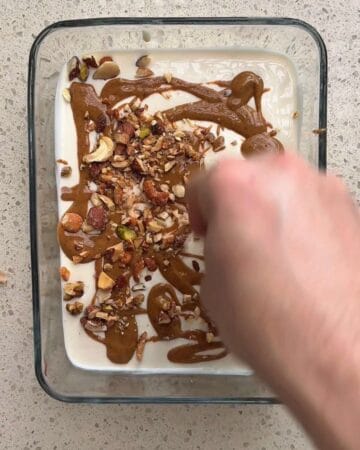 Adding chopped nuts and chocolate drizzle to homemade ice cream in a glass dish.