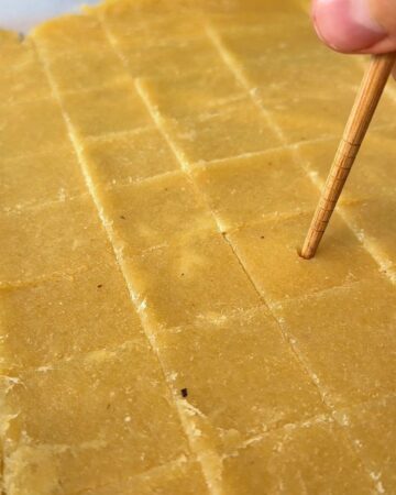 Close-up of homemade cheez-it squares being cut with a wooden stick.