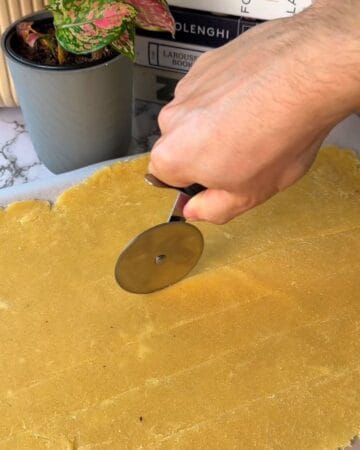 Person cutting cheez it dough with a round cutter for homemade crackers.