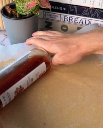 Person rolling out homemade cheez it dough with a hand and a bottle.