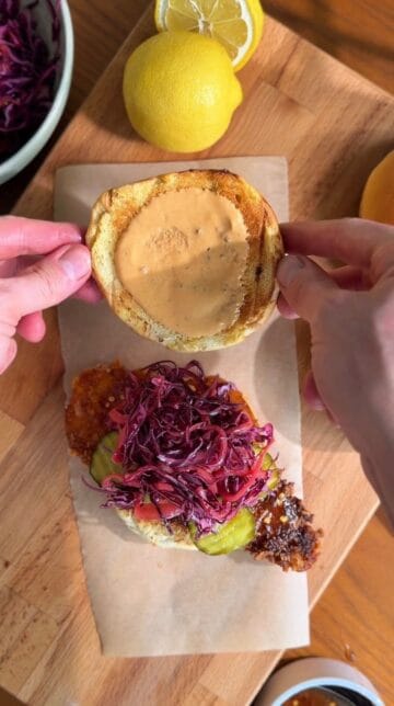 Building a hot honey chicken sandwich on toasted brioche bun with pickled slaw and dill pickles