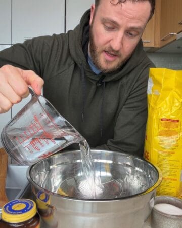 Chef Josh pouring water into mixing bowl for shaggy no knead cheddar bread dough with instant yeast and shredded cheddar
