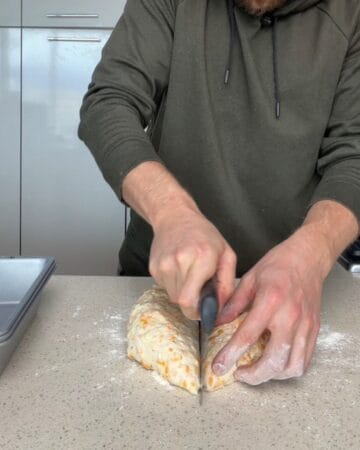 cheddar bread dough divided and rolled into two log shaped loaves on a floured surface