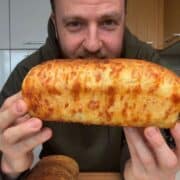 Chef Josh holding a large cheesy bread loaf in a kitchen setting.