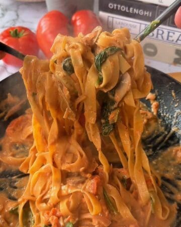 Delicious one pan creamy salmon pasta topped with fresh basil and tomato sauce, served hot on a black plate