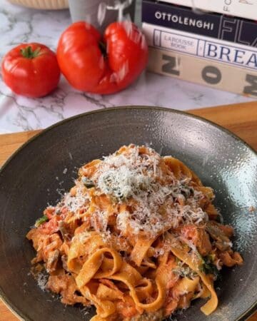 Delicious creamy one pan salmon pasta served with grated cheese, fresh tomatoes, and a cozy kitchen setting.
