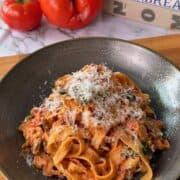Creamy one pan salmon pasta topped with grated cheese, served in a black bowl with fresh tomatoes.