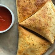 freshly baked pepperoni pizza pockets on a metal tray, with golden brown tortilla crust and marinara for dipping