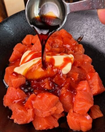 Salmon cubes being marinated with soy sauce and mayonnaise in a black bowl for the making of salmon sushi cups